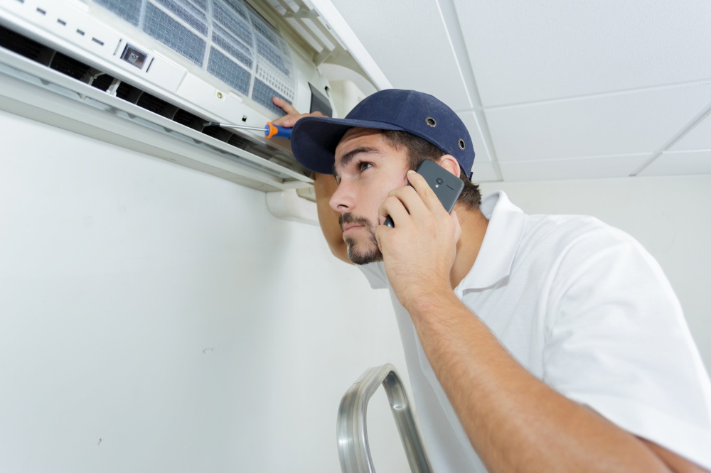 young handyman repairing air conditioning system calling for help
