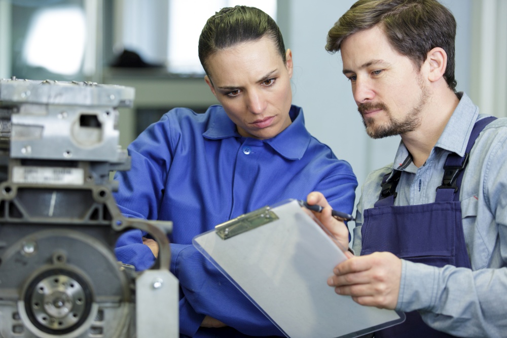 portrait of engineer and apprentice examining component in factory