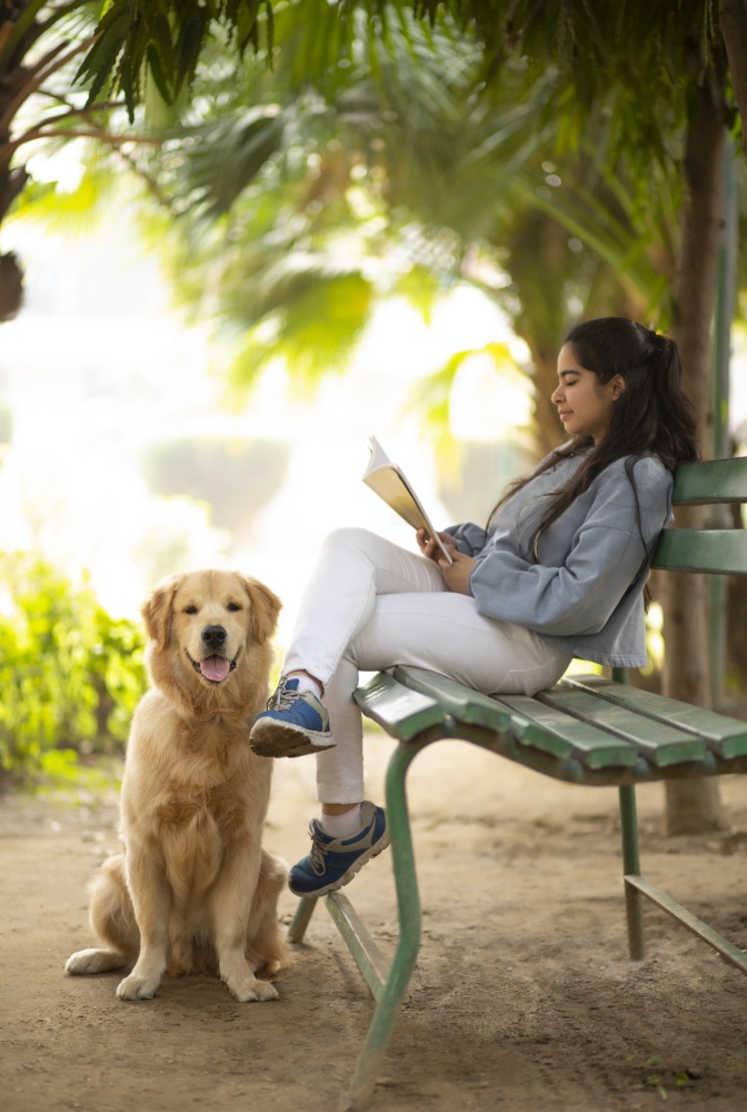 A PET DOG LOOKING AT CAMERA WHILE YOUNG GIRL HAPPILY READS BOOK