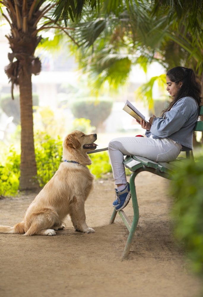 A YOUNG GIRL READING BOOK WHILE PET DOG OBEDIENTLY LOOKING AT HER