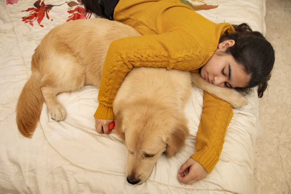 A PET DOG AND YOUNG GIRL SLEEPING TOGETHER ON BED