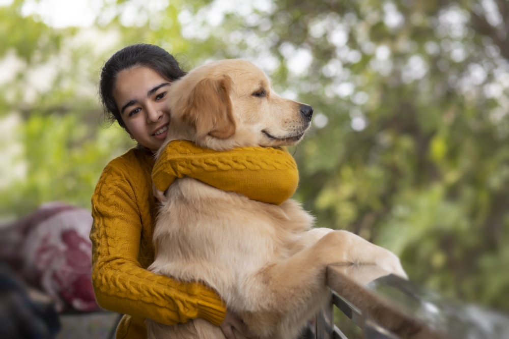 A HAPPY TEENAGER LOOKING AT CAMERA WHILE HUGGING PET DOG