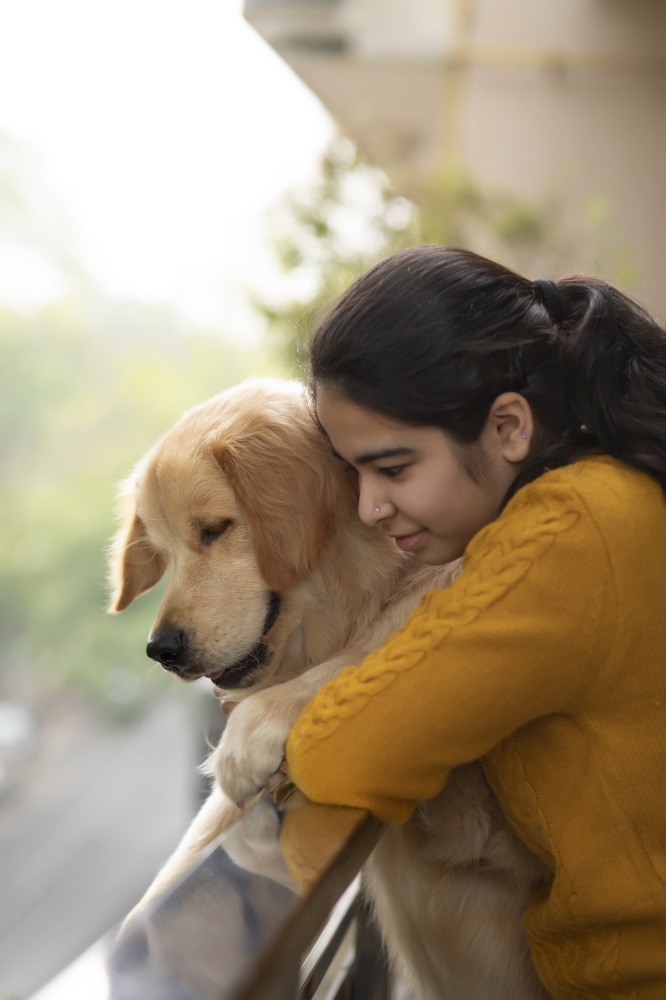 A PET DOG AND YOUNG GIRL LEANING OVER RAILING AND HAPPILY LOOKING DOWN