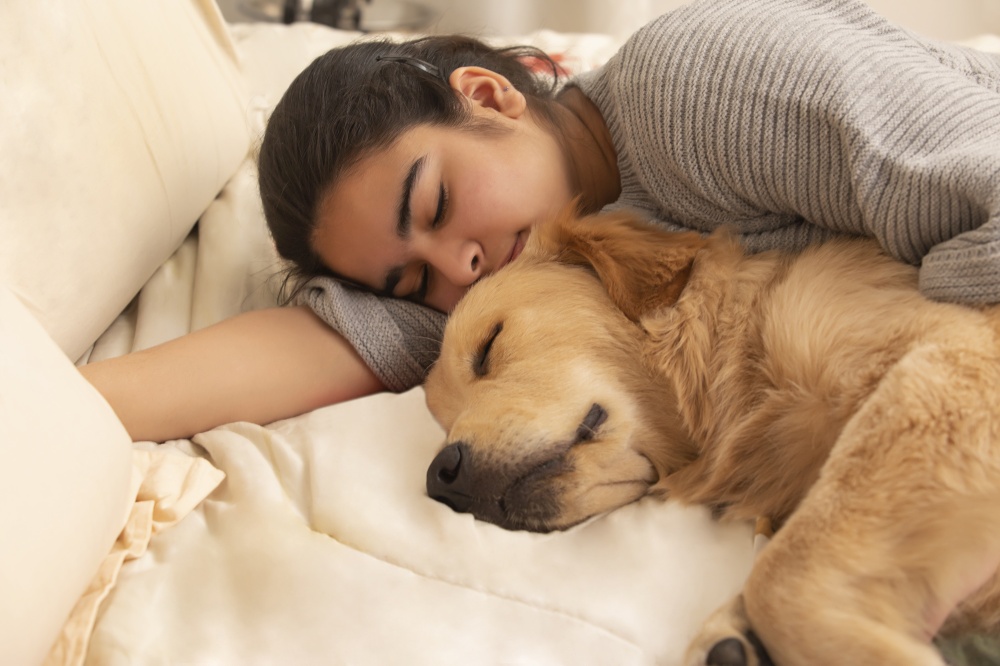A PET DOG AND TEENAGER SLEEPING TOGETHER ON BED