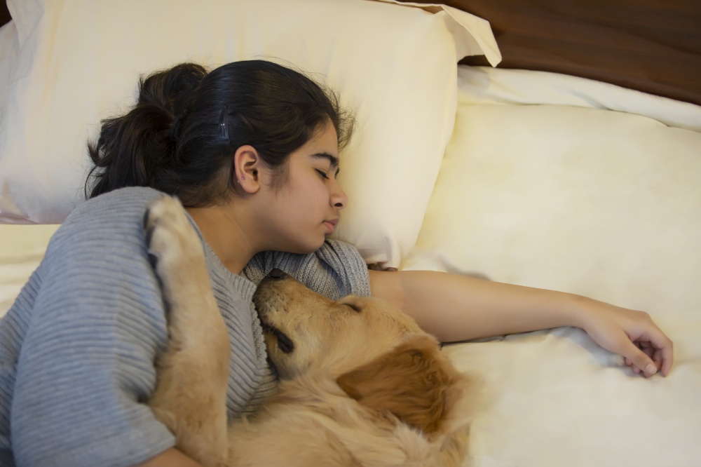 A YOUNG GIRL AND PET DOG COMFORTABLY SLEEPING TOGETHER ON BED