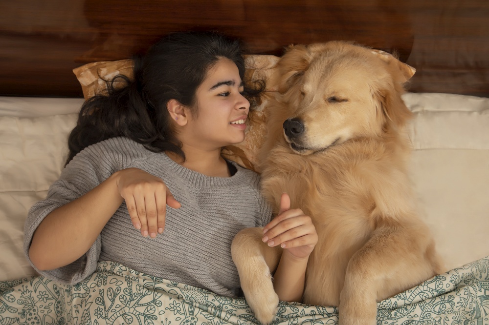 A HAPPY YOUNG GIRL AND PET DOG LYING ON BED AND PLAYING WITH EACH OTHER