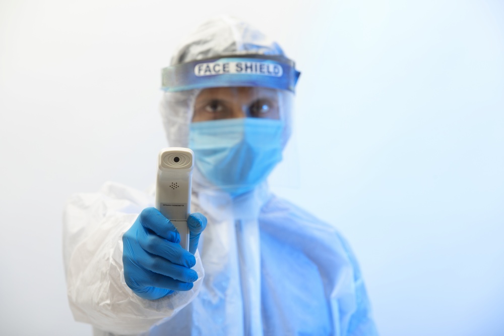 Man in a protective suit with an infrared thermometer gun in his hand