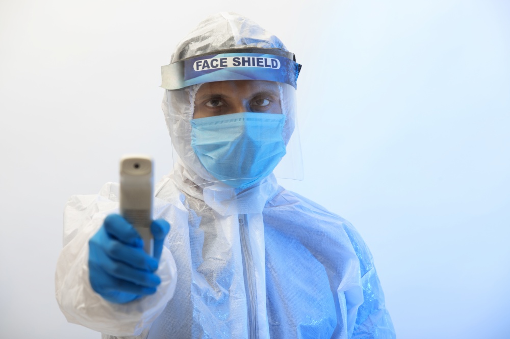 Man in a protective suit with an infrared thermometer gun in his hand