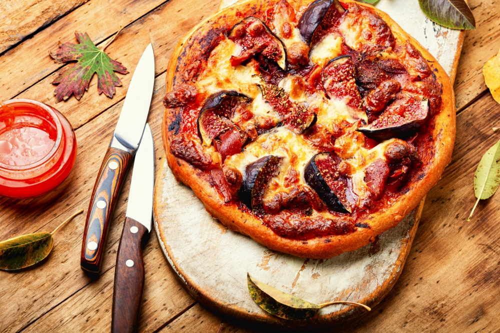 Appetizing pizza with prosciutto and autumn fruit, figs on wood background.. Meat pizza with figs.