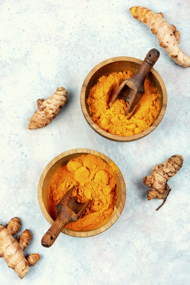Fresh turmeric root in wooden bowl and turmeric powder. Top view.. Turmeric root and turmeric powder.