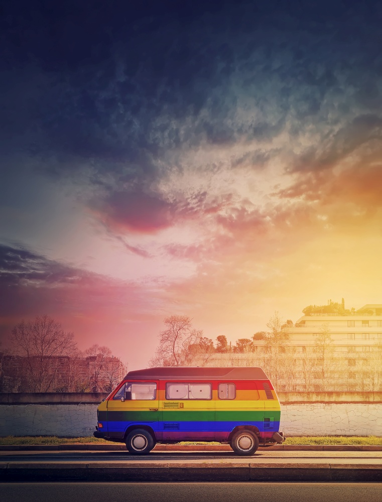 Rainbow painted vintage van parked on the edge of the street in the sunset light background. Lgbtq colors, pride symbol bus