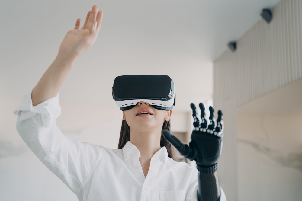 Disabled girl in virtual reality glasses touching 3d objects by robotic hand, testing new bionic prosthetic arm. Contemporary high tech in medicine and healthcare. Rehabilitation after limb loss.. Disabled girl in vr glasses testing new bionic prosthetic arm. Rehabilitation after limb loss