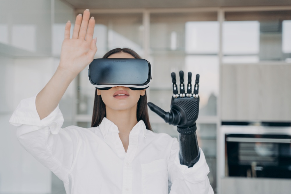 Female wearing virtual reality glasses interacting with augmented cyberspace, touching objects by bionic prosthetic arm, training to use artificial limb, high tech robotic hand. Medical technologies.. Female in virtual reality glasses training to use bionic prosthetic arm. Medical technologies