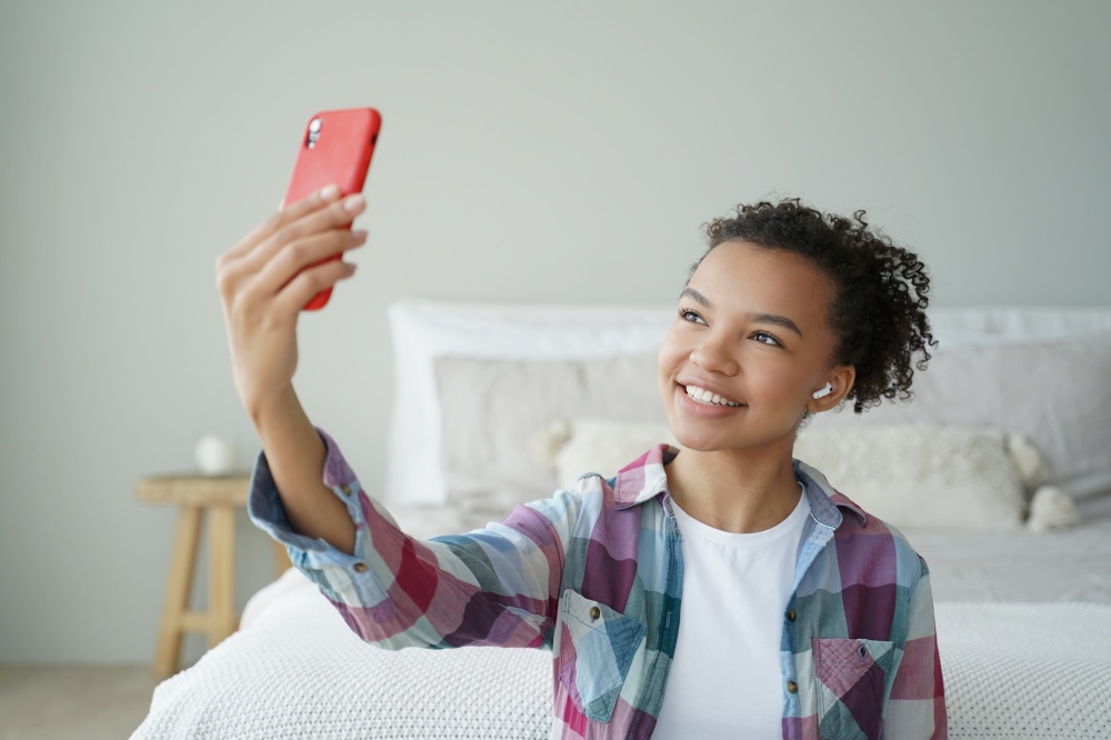 Mixed race teen girl blogger chatting online by phone video call, using modern mobile apps at home. Friendly smiling biracial teenager lady holding smartphone, takes a selfie photography.. Mixed race teen girl blogger chatting online by phone video call, using modern mobile apps at home