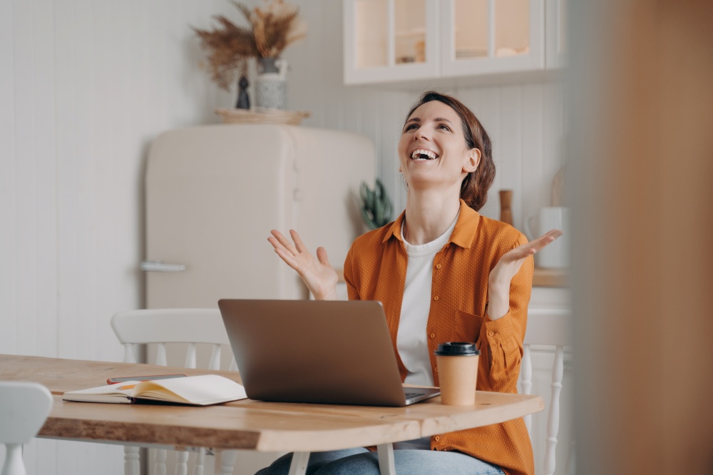 Excited hispanic woman got email with perfect good news, gesturing, sitting at laptop in kitchen. Euphoric joyful female freelancer celebrating unexpected surprise, job offer, promotion at work.. Happy hispanic woman got email with perfect good news, gesturing, sitting at laptop in kitchen