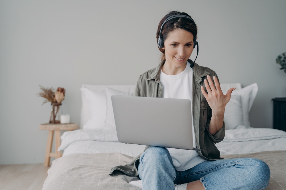 Hispanic woman coach trainer in headset conducts online consultation, webinar by video call on laptop, speak before virtual audience. Confident businesswoman consult client distantly, working at home.. Female coach in headset conducts online consultation, webinar by video call on laptop at home