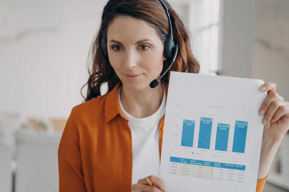 Marketing professional woman in headset talking to coworkers on video call, presenting graph reports, showing, explaining chart. Female employee, manager business coach speaking at online meeting.. Female business coach in headset speaking at online meeting on video call, showing, explaining chart