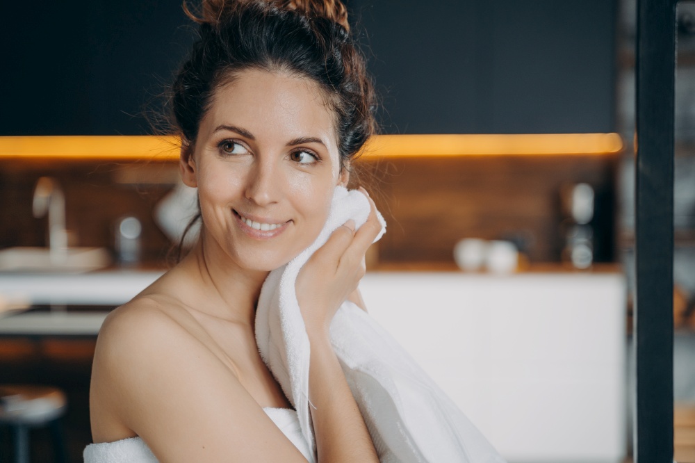 Smiling hispanic woman wiping face with white cotton towel after shower, happy pretty female with naked shoulder enjoying her fresh glowing skin after skincare beauty morning routine at home.. Smiling hispanic girl wiping face by towel enjoy fresh glowing skin after skincare treatment at home