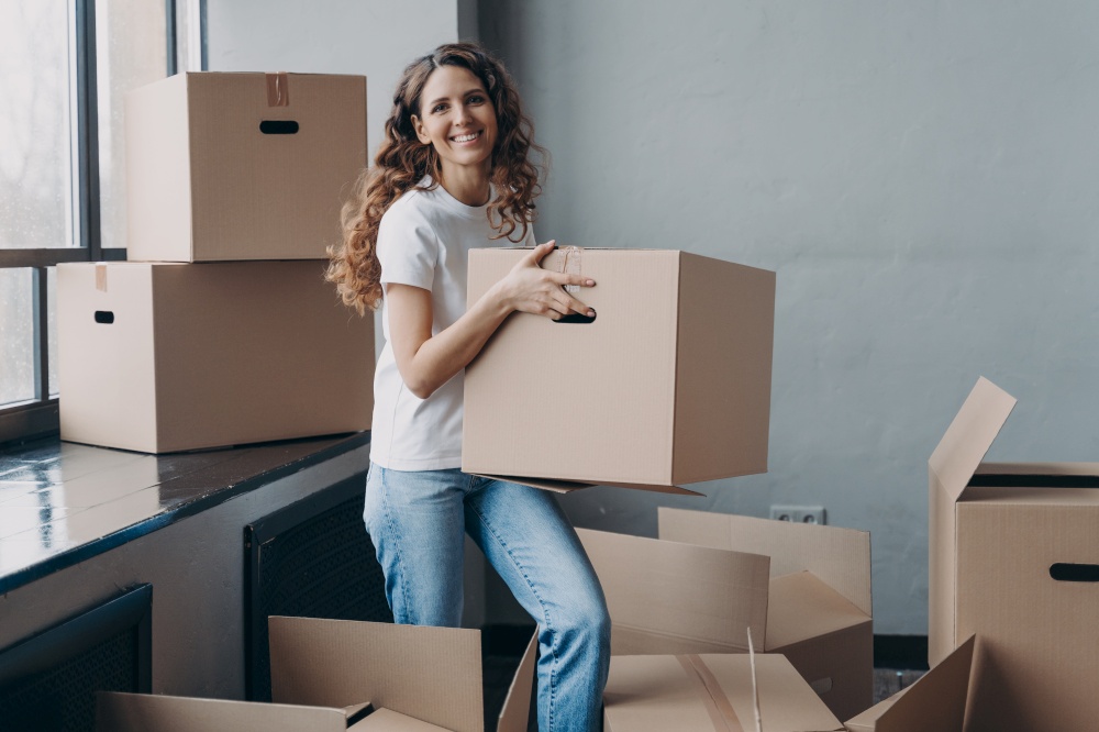 Excited latina female homeowner tenant carrying cardboard box with personal things on moving day. Happy woman packing belongings for relocation to new home apartment. Real estate rental, mortgage.. Excited girl carrying carton box with things for relocation to new home apartment. Mortgage, moving