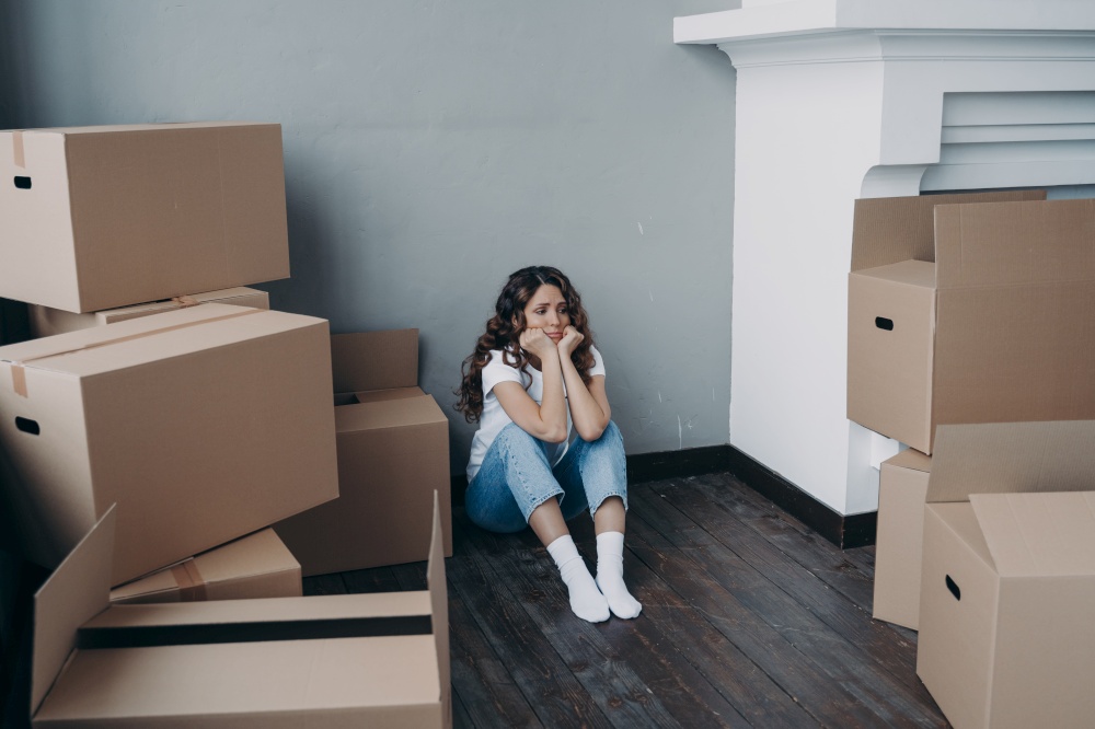 Upset young woman sitting with cardboard boxes with personal belongings goes through divorce, unsuccessful marriage, property division. Hispanic girl feel stress due to relocation. Eviction, move out.. Sad woman sitting with boxes goes through divorce, property division. Eviction, removal and stress