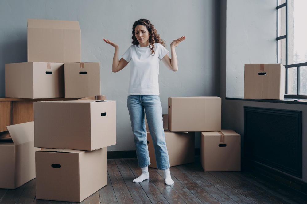Puzzled tired woman homeowner tenant spreading her hands standing among cardboard boxes in empty room, overworked spanish female feels exhausted of moving to new home. Hard relocation day.. Puzzled tired woman with cardboard boxes feels exhausted of moving to new home. Hard relocation day
