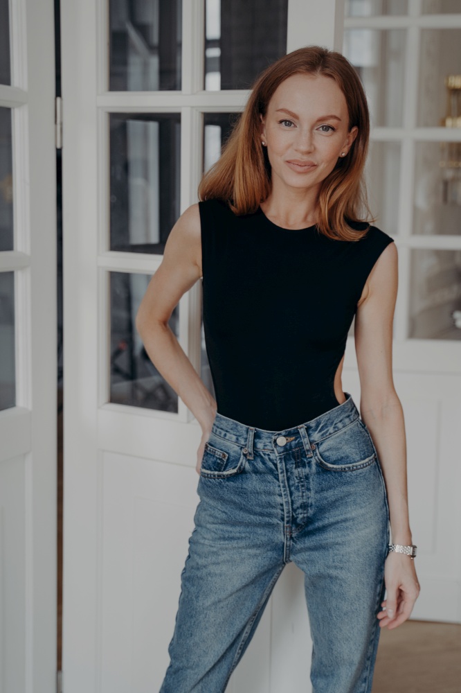 Portrait of happy confident middle age young woman. Pretty redhead european lady is standing near door window and smiling. Luxurious apartment interior. Concept of style, fashion and beauty.. Portrait of happy confident middle age young woman. Lady is standing near door window.