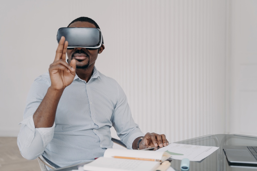 African american man architect designer in VR glasses working on project in virtual reality at office desk. Modern black male business person using modern high tech gadget for working in cyberspace.. African american man architect in VR glasses working on project in virtual reality at office desk