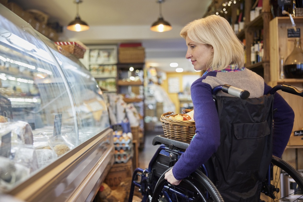 Woman In Wheelchair Shopping For Food In Delicatessen
