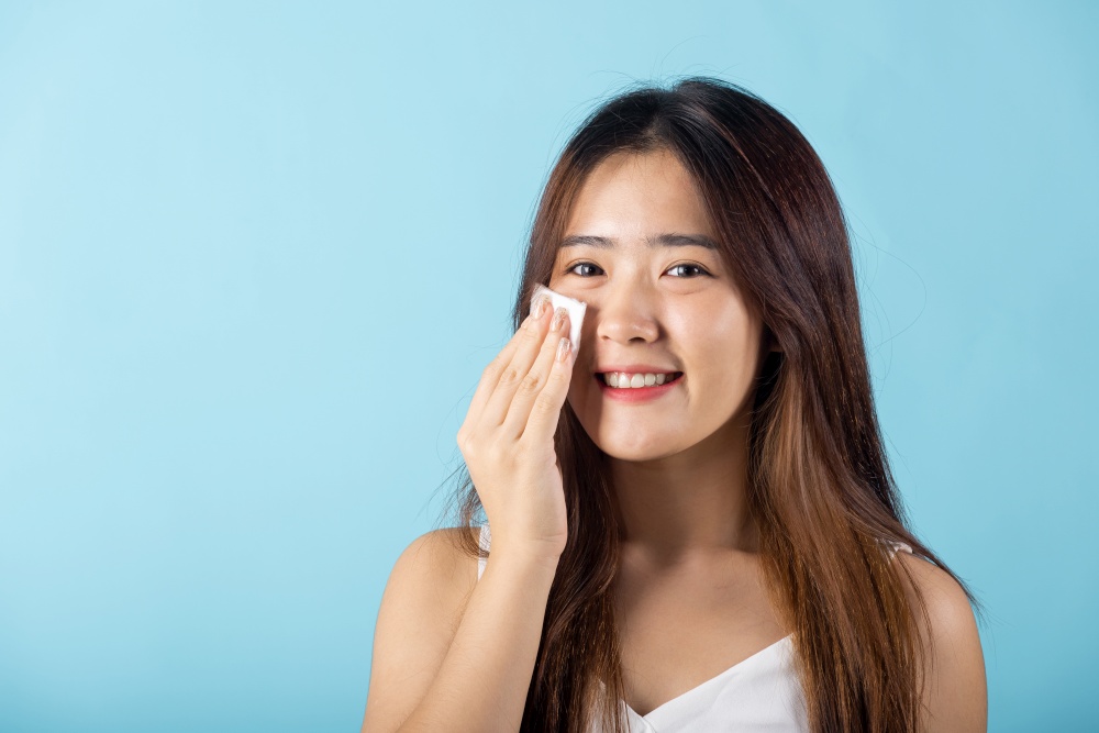 Facial Beauty Treatment Hygiene skin. Asian beautiful young woman removing cosmetic make up using pad cotton face cleaner disc, studio shot isolated on blue background, Happy female cleaning eyes