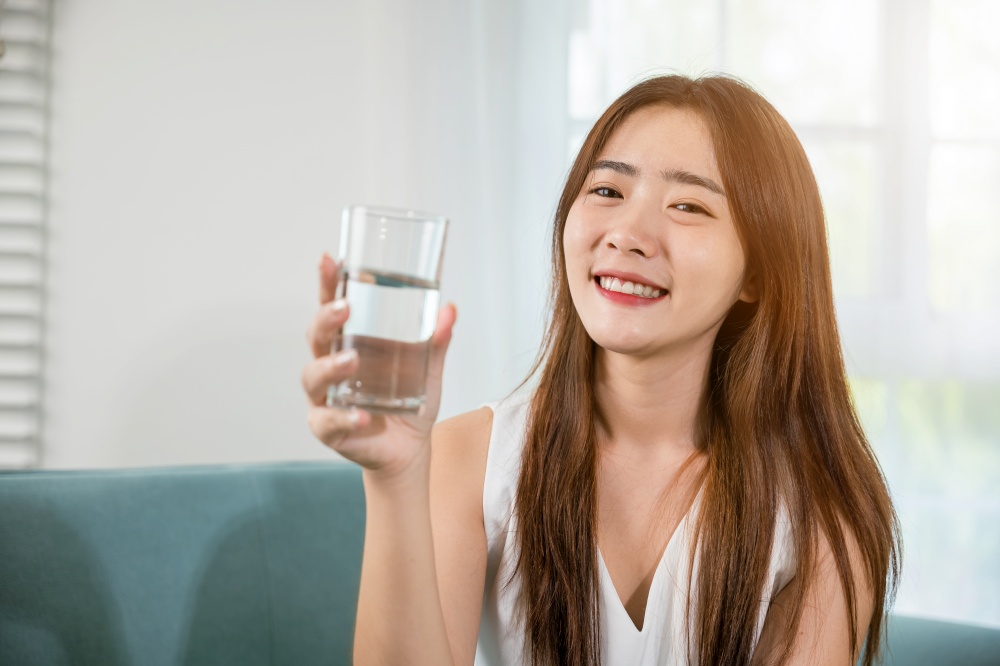 Portrait of Asian young woman holding drinking nature water on hand at home, Happy smiling female beauty with water glass for drink in living room, Healthy lifestyle