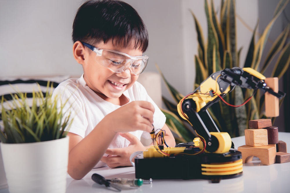 Happy Asian little kid boy using screwdriver to fixes screws robotic machine arm in home workshop, child learning repairing get lesson control robot arm, Technology future science education concept