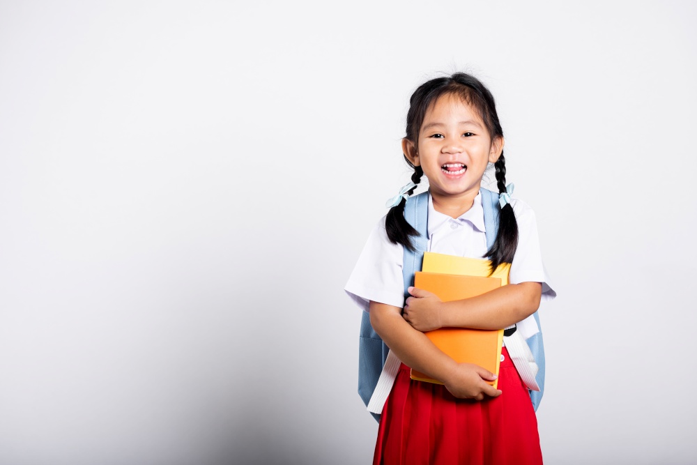 Asian adorable toddler smiling happy wear student thai uniform red skirt stand hold or hugging book in studio shot isolated on white background, Portrait little children girl preschool, Back to school