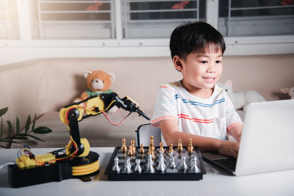 Asian little boy programming code to robot machine arm on laptop for play chess, STEM education E-learning, Funny children learning getting lesson control robot arm, Technology science education