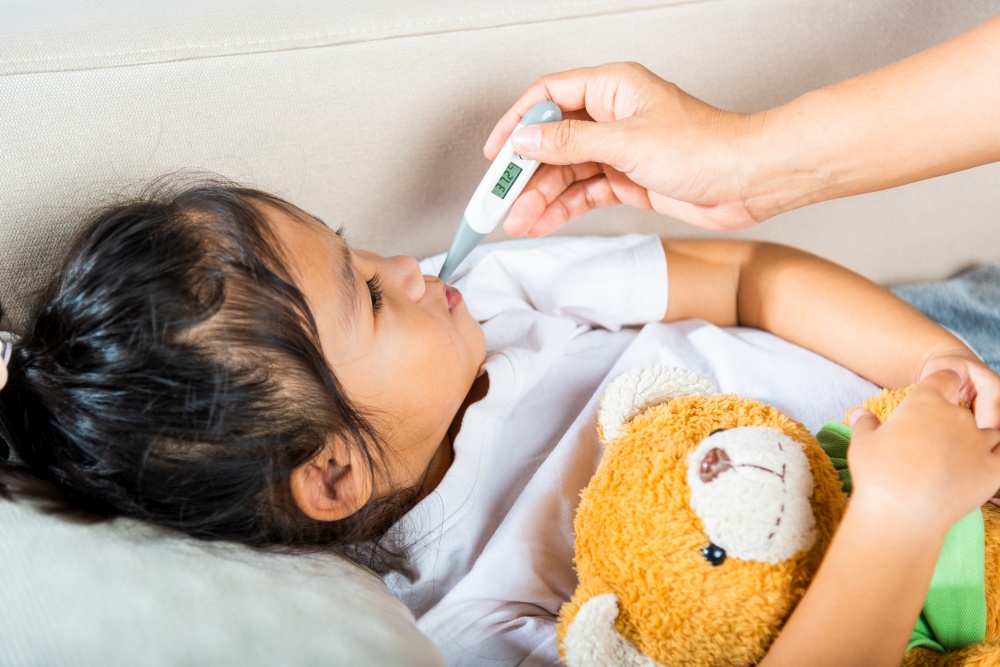 Sick kid. Mother checking temperature of her sick daughter with thermometer in mouth, child laying in bed taking measuring her temperature for fever and illness