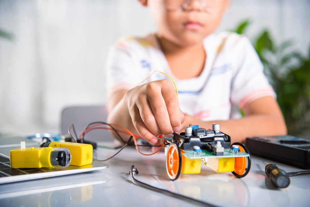 Asian kid boy plugging energy and signal cable to sensor chip with Arduino robot car, Little child remotely learn online with car toy, STEAM education AI technology course school learning lesson