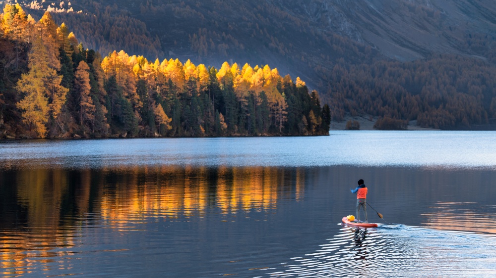 On paddleboard in mountain lake in autumn in solitude