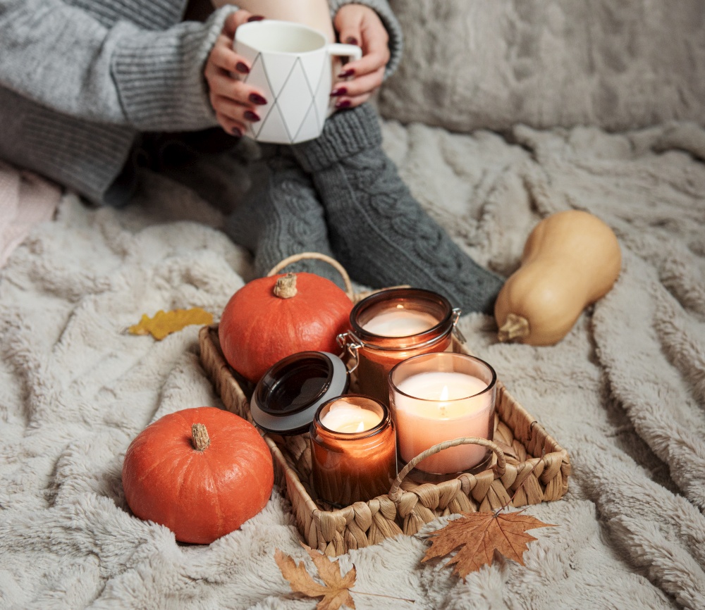 A girl in a sweater and knitted socks sits on a blanket. Cozy autumn concept. Pumpkins and candles on a tray near the girl.