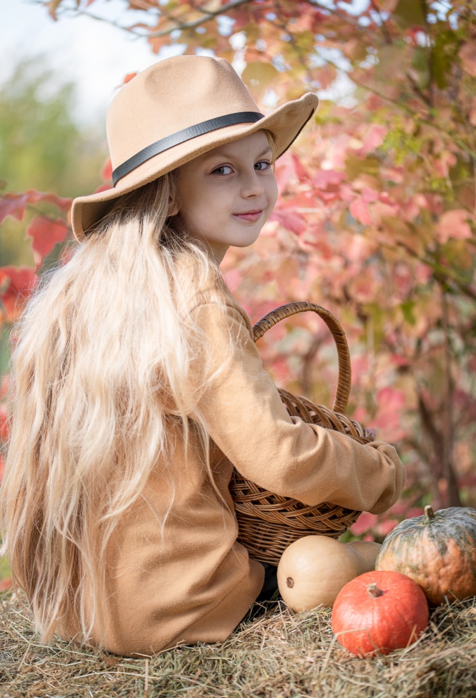 Little girls sitting among hay bales and pumpkins in the autumn garden