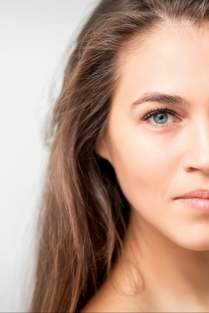 Half face portrait of young caucasian woman with natural make up and eyelash extensions looking at camera on white background. Face portrait of young caucasian woman