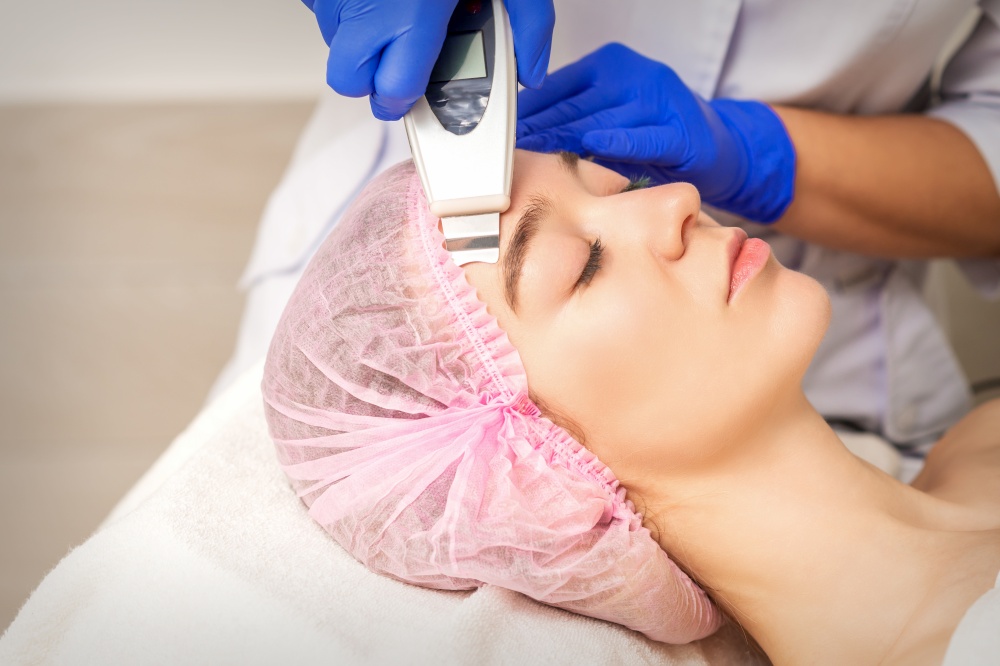 Young woman receiving facial skin cleaning by ultrasonic cosmetology face equipment in medical salon. Young woman receiving facial ultrasonic cleaning