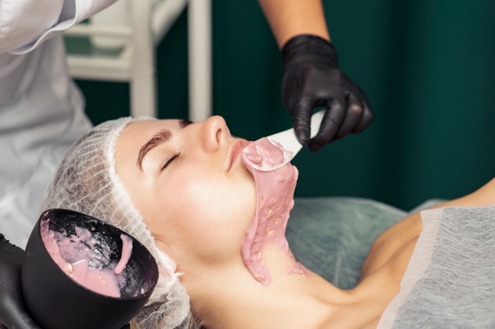 The cosmetologist applying an alginic mask to the face of a young woman in a beauty salon. Cosmetologist applying an alginic mask