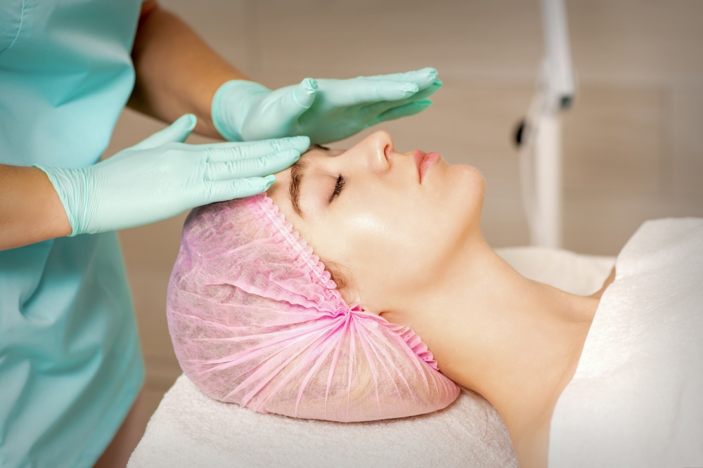 The woman is having cosmetic treatment during cosmetologist in medical gloves are touching the female face at the spa salon. The woman is having cosmetic treatment during cosmetologist in medical gloves are touching the female face at the spa salon.