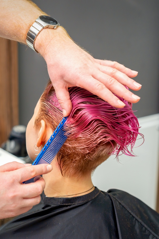 Hands of hairdresser combing hair making short pink hairstyle for a young caucasian woman in a beauty salon. Hands of hairdresser combing hair making short pink hairstyle for a young caucasian woman in a beauty salon.
