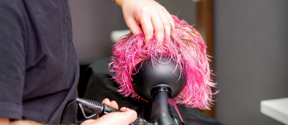 Hair Stylist making hairstyle using hair dryer blowing on wet custom pink hair at a beauty salon. Hair Stylist making hairstyle using hair dryer blowing on wet custom pink hair at a beauty salon.