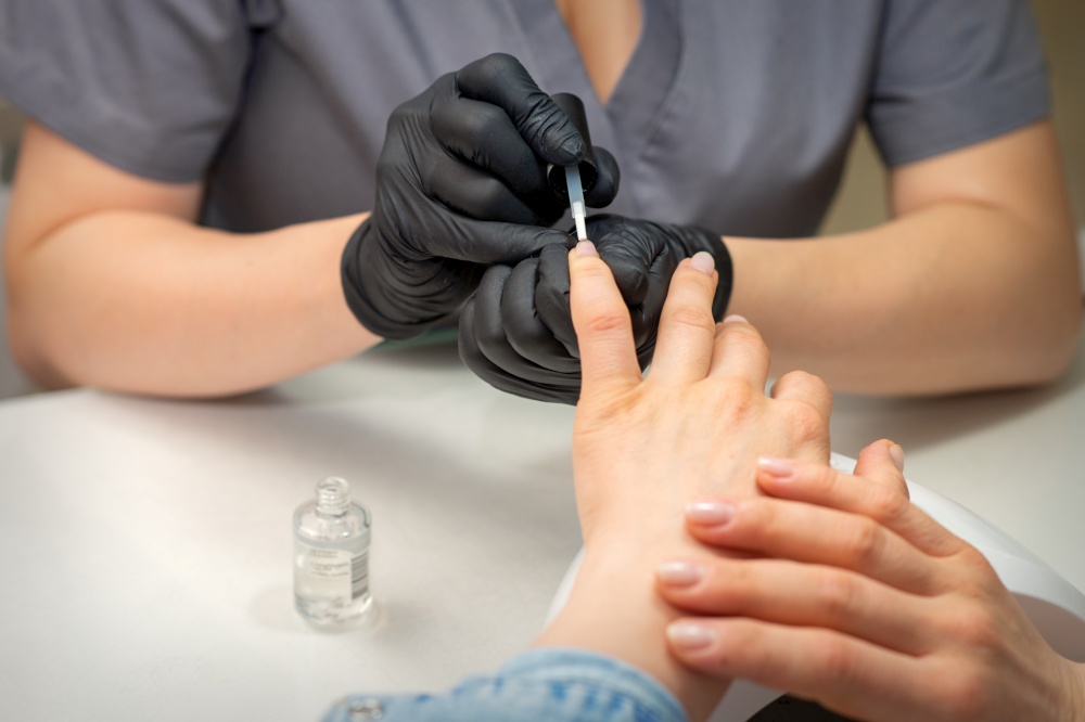 Painting female nails. Hands of manicurist in black gloves is applying transparent nail polish on female nails in a manicure salon. Painting female nails. Hands of manicurist in black gloves is applying transparent nail polish on female nails in a manicure salon.