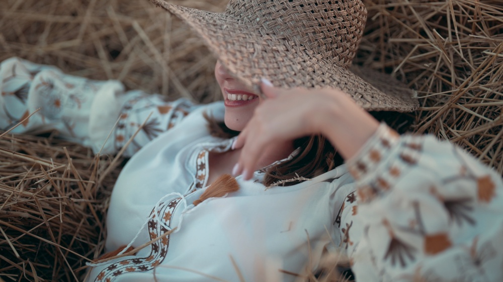 Pretty woman in straw hat and embroidered blouse smiling lying on hay in countryside at sunset. Rural nature, haystack, vacation, relax and harvest concept. High quality photo. Pretty woman in straw hat and embroidered blouse smiling lying on hay in countryside at sunset. Rural nature, haystack, vacation, relax and harvest concept.