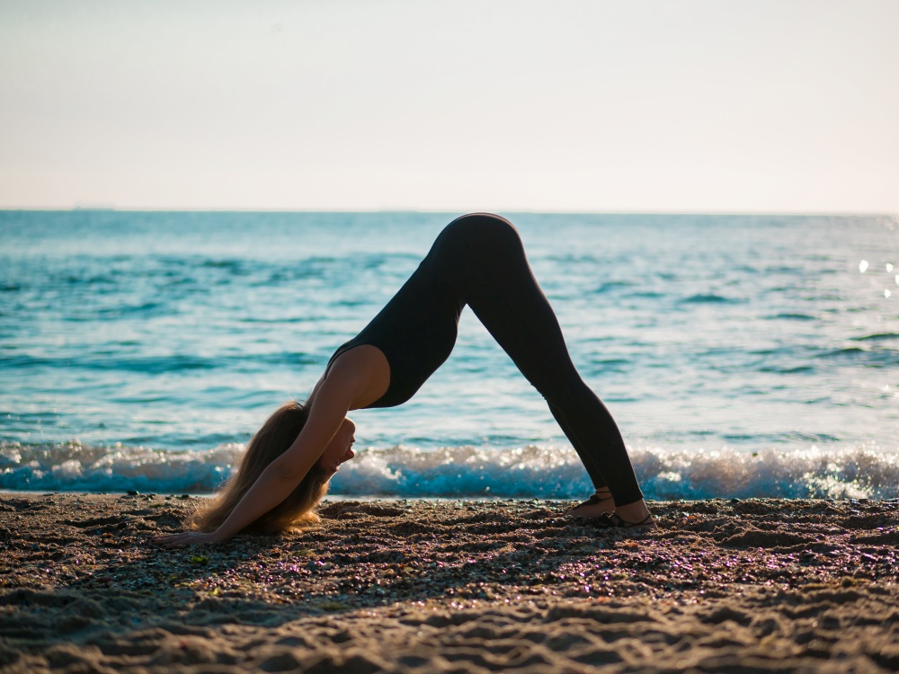 Beautiful young woman practicing morning yoga on sand sea beach. Surya Namaskar - Sun Greetings.