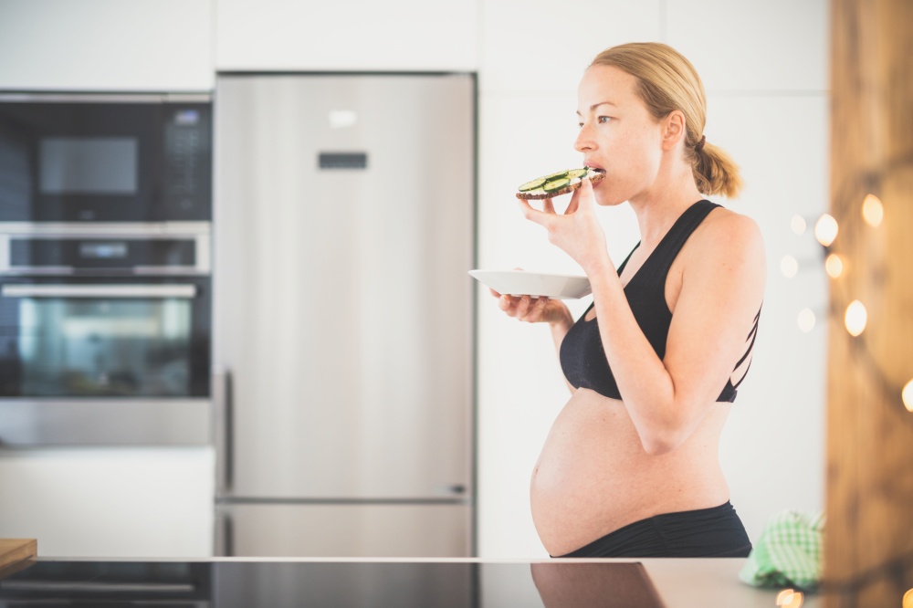Beautiful sporty fit young pregnant woman having a healthy snack in home kitchen. Healty lifestyle concept. Beautiful sporty fit young pregnant woman having a healthy snack in home kitchen. Healty lifestyle concept.