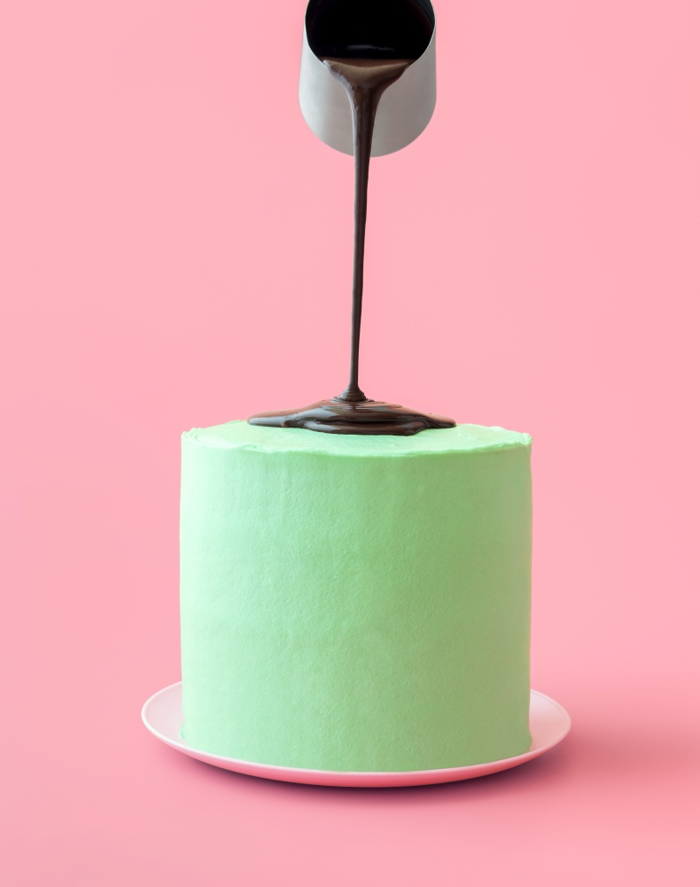 Pouring dark chocolate over frosted cake, minimalist on a pink background. Homemade mint-flavored cake with dark chocolate topping