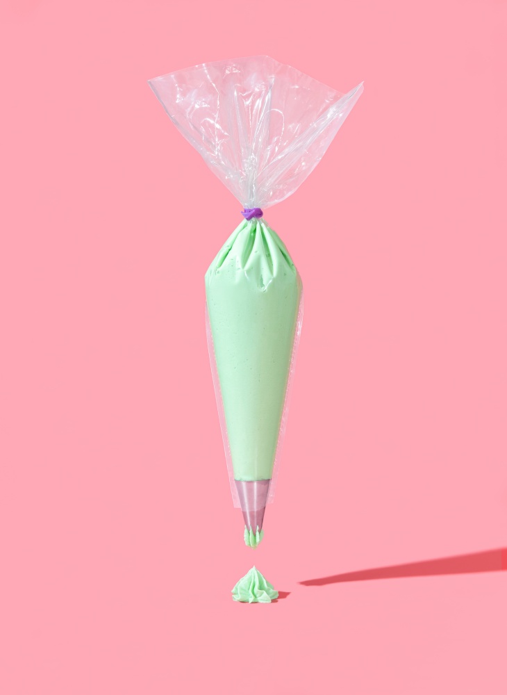 Pastry bag full of green buttercream frosting, minimalist on a pink background. Flying frosting bag in bright light on a colorful table.